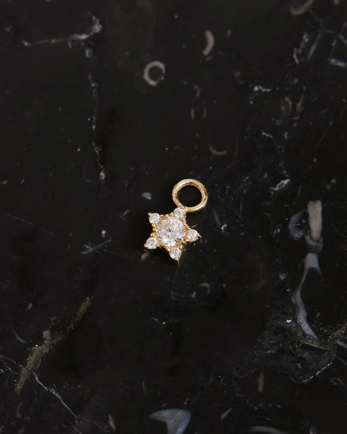 Produktfoto des Stern Ohrring Charms Gold auf schwarzen Mamor liegend