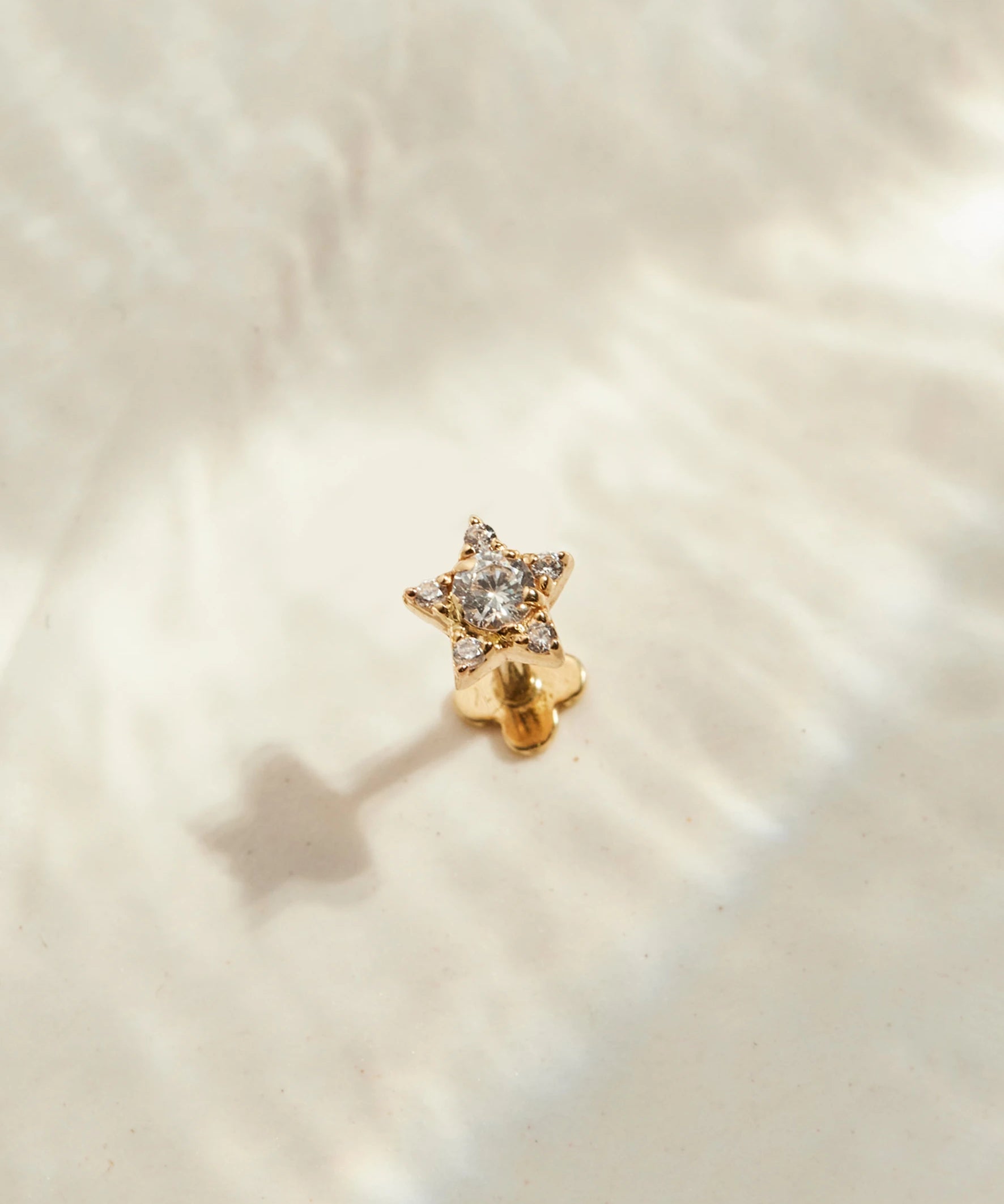 Stern Piercing Gold steht auf einer beigen Oberfläche
