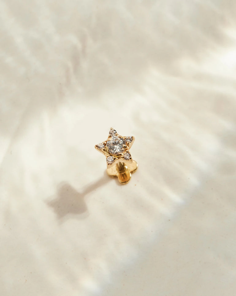 Stern Piercing Gold steht auf einer beigen Oberfläche